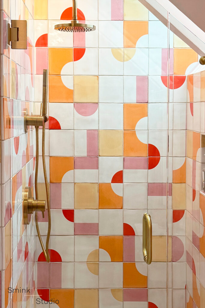 Shower of white Smink Studio handmade ceramic tiles with pink, orange, yellow and red half-circle screen-printed colours, with brass rain shower and fittings.
