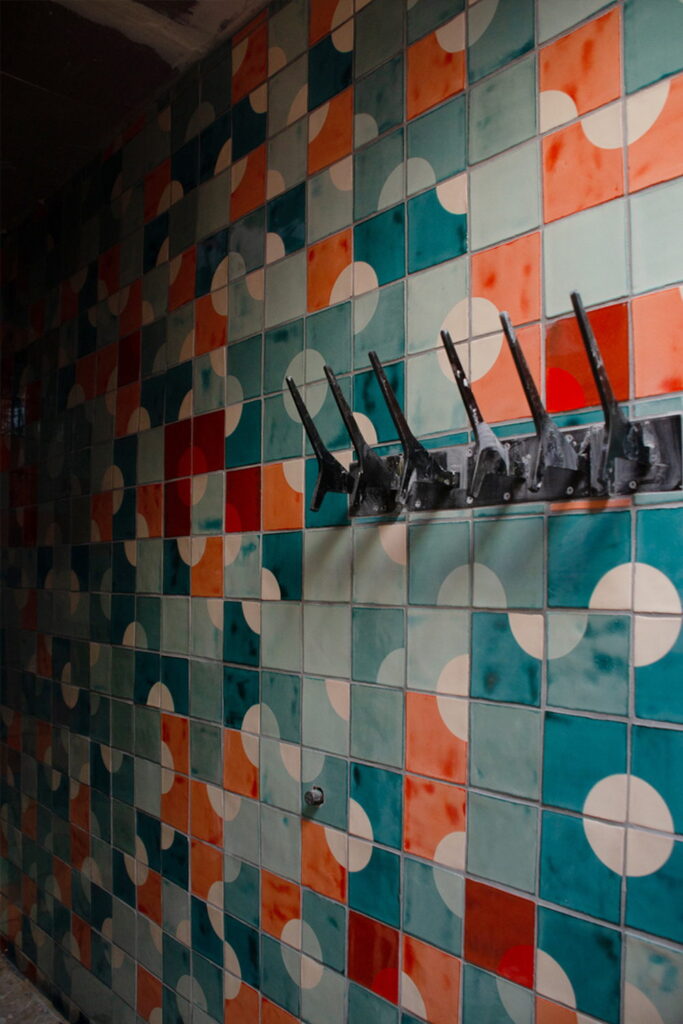 Wall of Smink Studio handmade ceramic tiles in teal, orange and cream with a circle pattern in screen-printed colours, fitted with a row of black coat hooks.