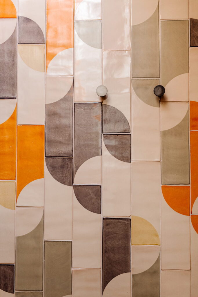 Smink Studio handmade ceramic tiles in cream, orange and olive with a half-circle pattern in screen-printed colours, set with two round wall knobs.