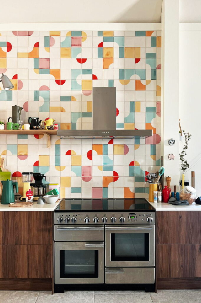 Kitchen of Smink Studio handmade ceramic tiles in cream with red, teal, mustard and coral half-circle screen-printed colours, behind a stainless range with walnut cabinets.