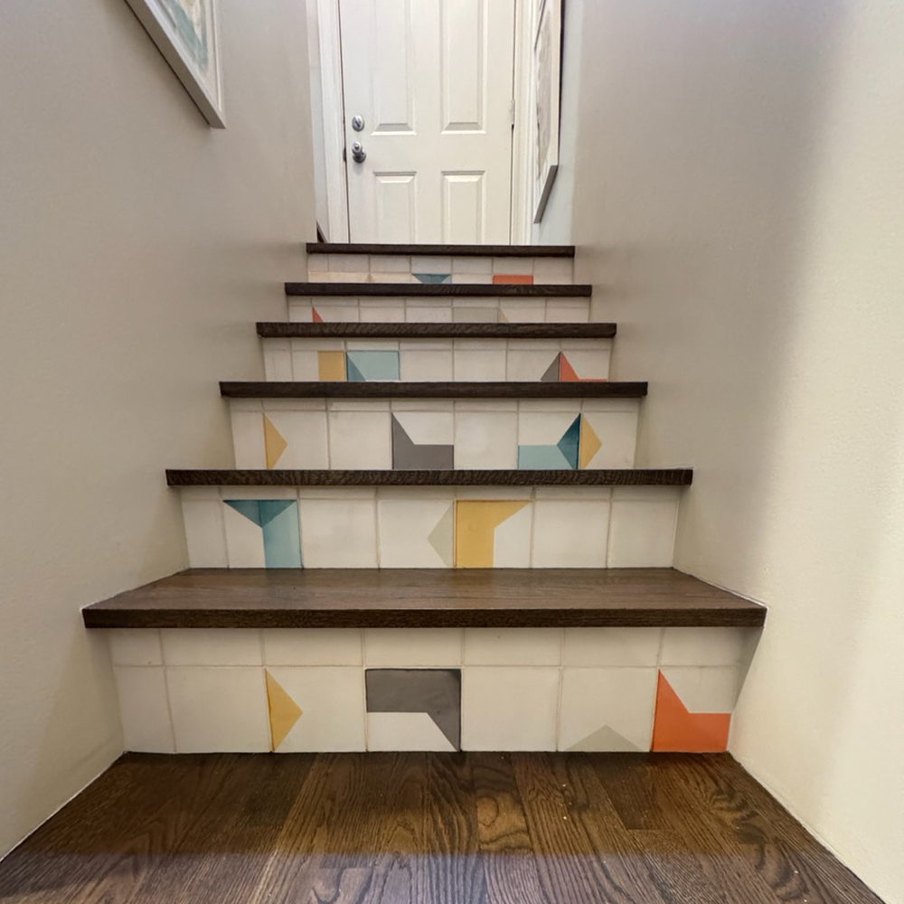 Staircase risers tiled in white Smink Studio handmade ceramic tiles with teal, mustard, grey and orange geometric screen-printed colours, between oak treads.