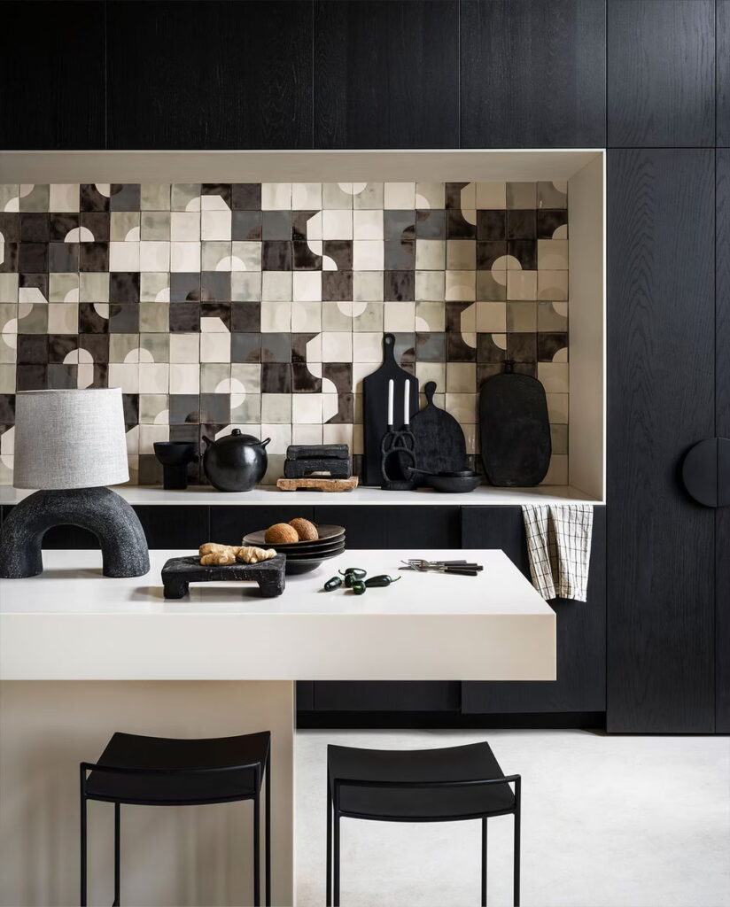Kitchen niche of black, cream and grey Smink Studio handmade ceramic tiles with half-circle screen-printed colours and metallic-lustre glaze, with black cabinets and dark styling.