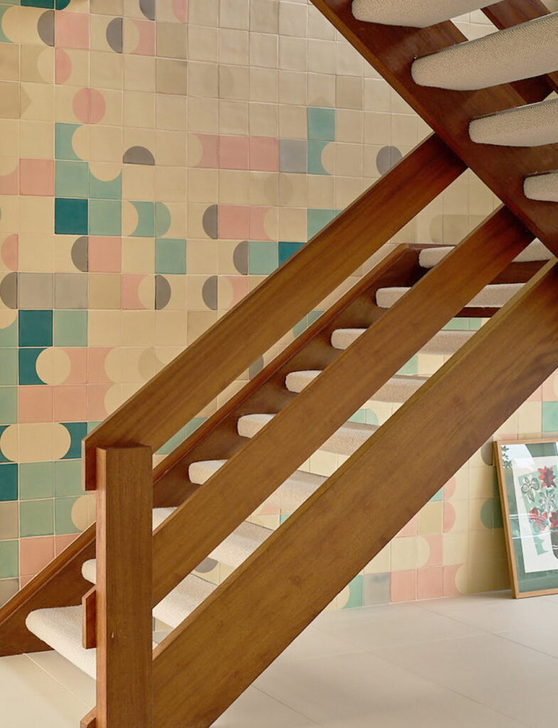 Understairs wall of Smink Studio handmade ceramic tiles in cream, sage-green, pink and grey half-circle screen-printed colours, beside a timber staircase.