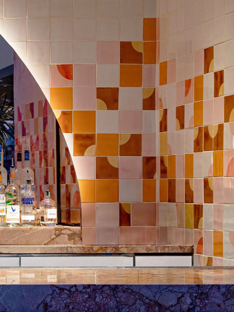 Hotel bar backed by Smink Studio handmade ceramic tiles in pink, terracotta, orange and cream half-circle screen-printed colours with a curved edge, above a marble bar.