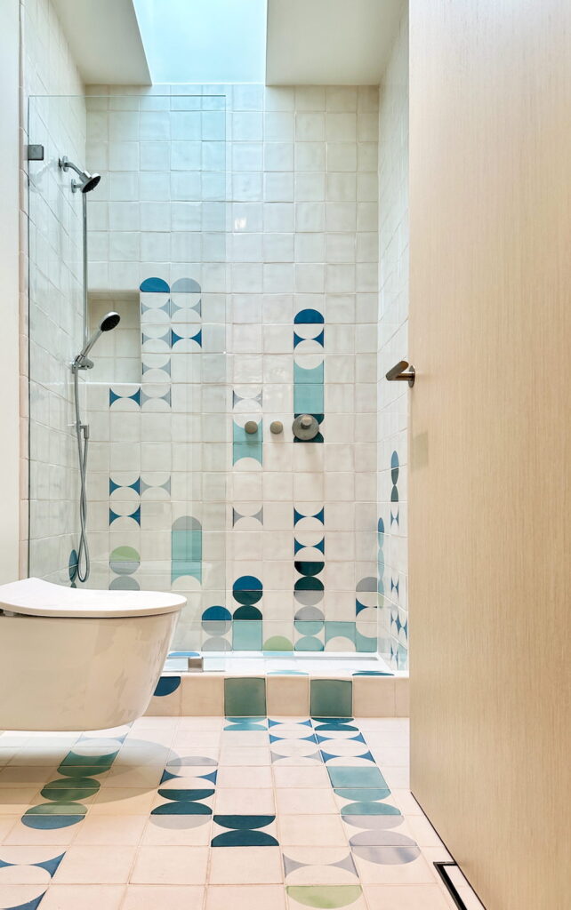 Bathroom of white Smink Studio handmade ceramic tiles with blue, teal and green lens-shaped screen-printed colours in the shower and matching floor, with a freestanding bath.