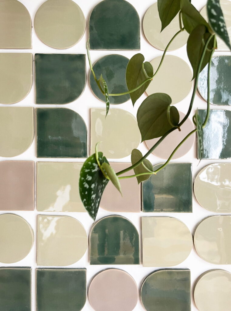 Flat-lay of Smink Studio handmade ceramic tiles in sage-green, olive, cream and blush pink shapes, with a trailing pothos vine.