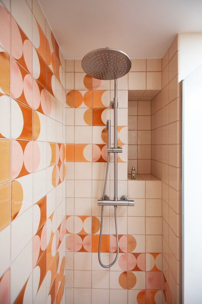 Shower of Smink Studio handmade ceramic tiles in cream, pink and orange half-circle screen-printed colours, with a chrome rain shower and niche.