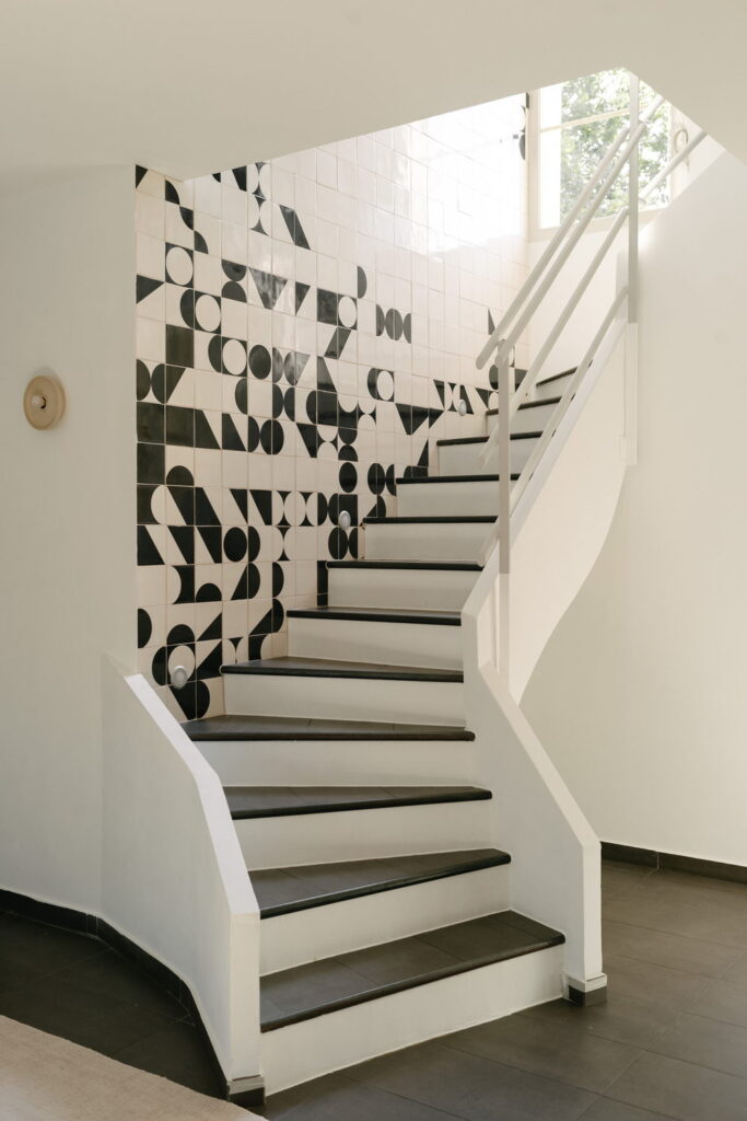 Staircase with a feature wall of black and white Smink Studio handmade ceramic tiles in geometric screen-printed colours, beside white winder stairs.