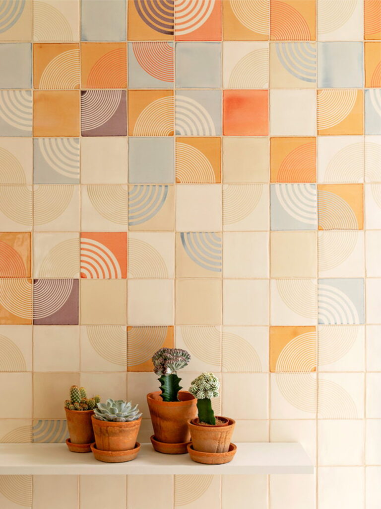 Detail of Smink Studio handmade ceramic tiles in cream, orange, blue and mauve with concentric-arc screen-printed colours, with terracotta pots and cacti.