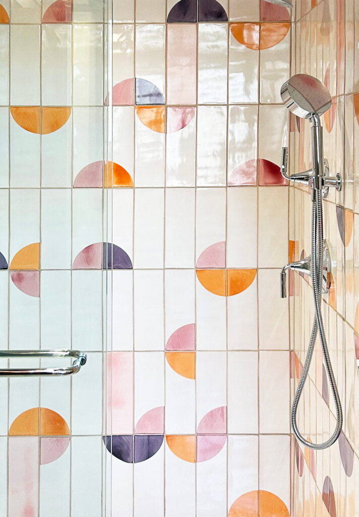 Shower of cream Smink Studio handmade ceramic tiles with pink, orange and purple half-circle screen-printed colours, with a chrome shower.