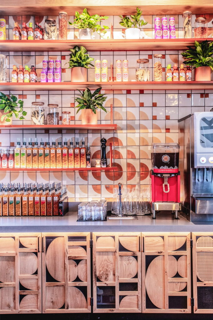 Restaurant bar of Smink Studio handmade ceramic tiles in cream, terracotta and coral half-circle screen-printed colours, above oak cabinets with carved half-circle fronts.